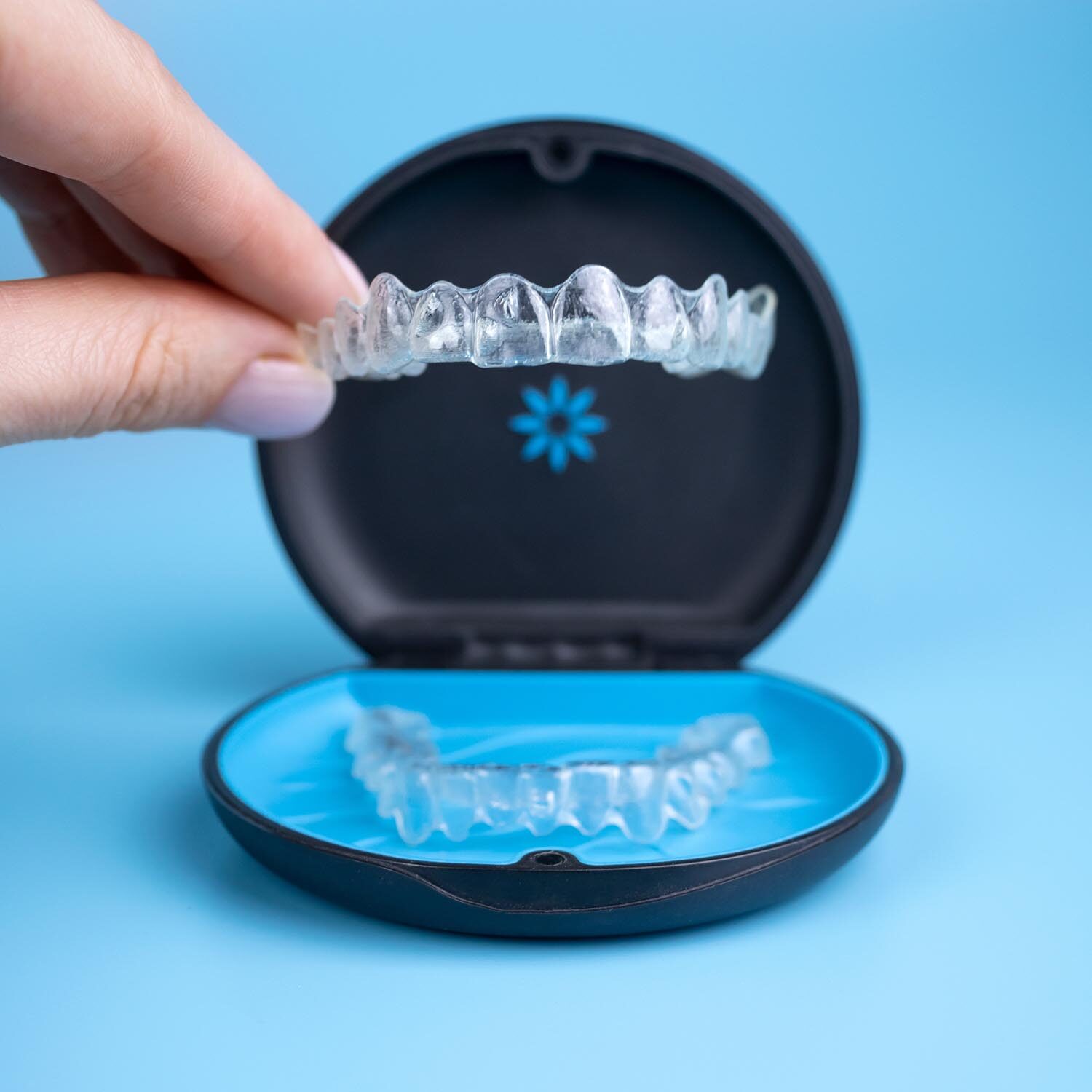 Woman holding invisalign transparent retainers with a box on the table, flatlay top view. Selective focus.